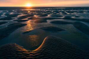 Zonsondergang boven een strand bij eb.