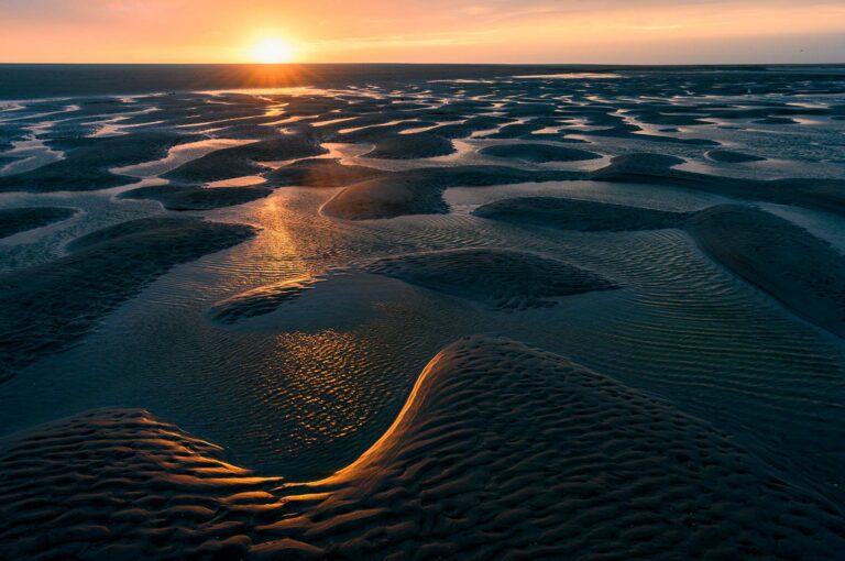 Zonsondergang boven een strand bij eb.