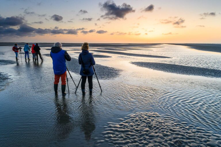 Fotografen met statieven op het strand bij ondergaande zon